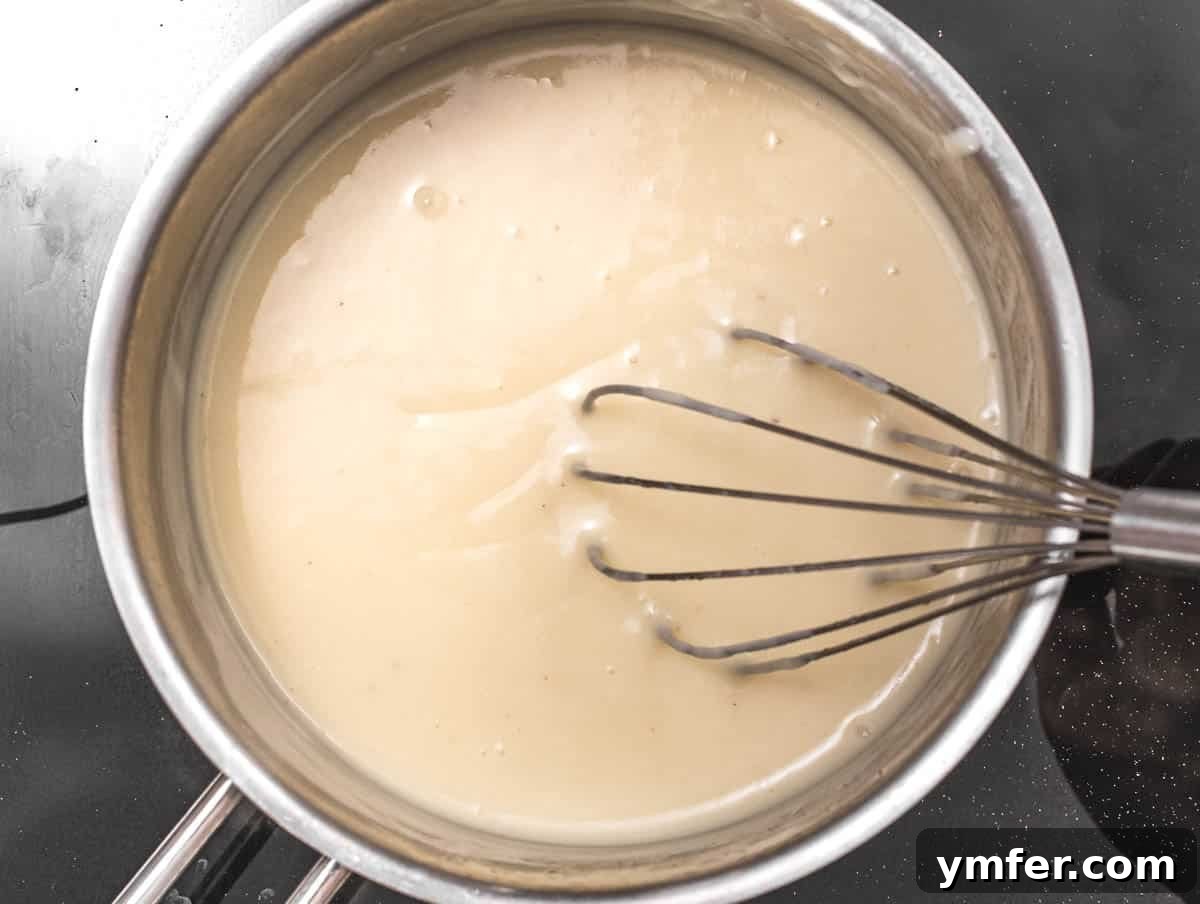 Luscious Vegan Cream Sauce 6 Smooth and creamy vegan white sauce thickening in a saucepan, being stirred with a whisk.