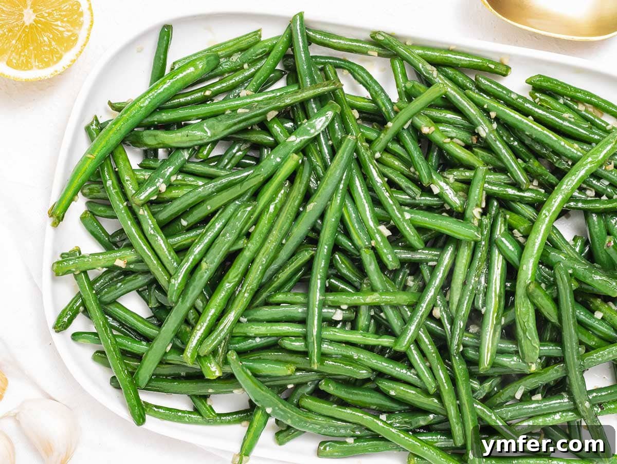 Flavorful Sautéed Green Beans 10 A serving of sautéed green beans garnished with lemon wedges and fresh garlic slices, presented on a white plate
