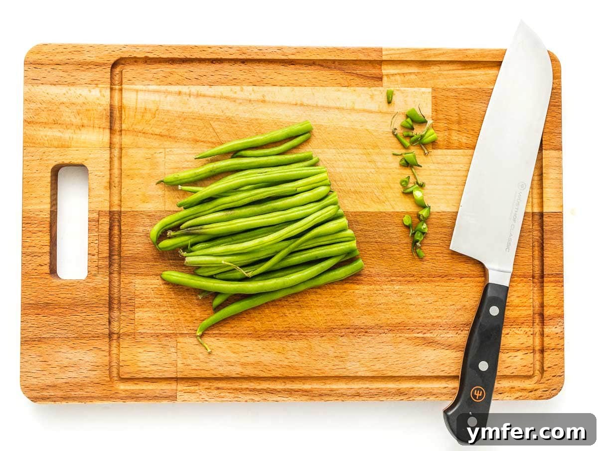 Flavorful Sautéed Green Beans 5 A chef's knife carefully trimming the ends of a bunch of fresh green beans on a wooden cutting board