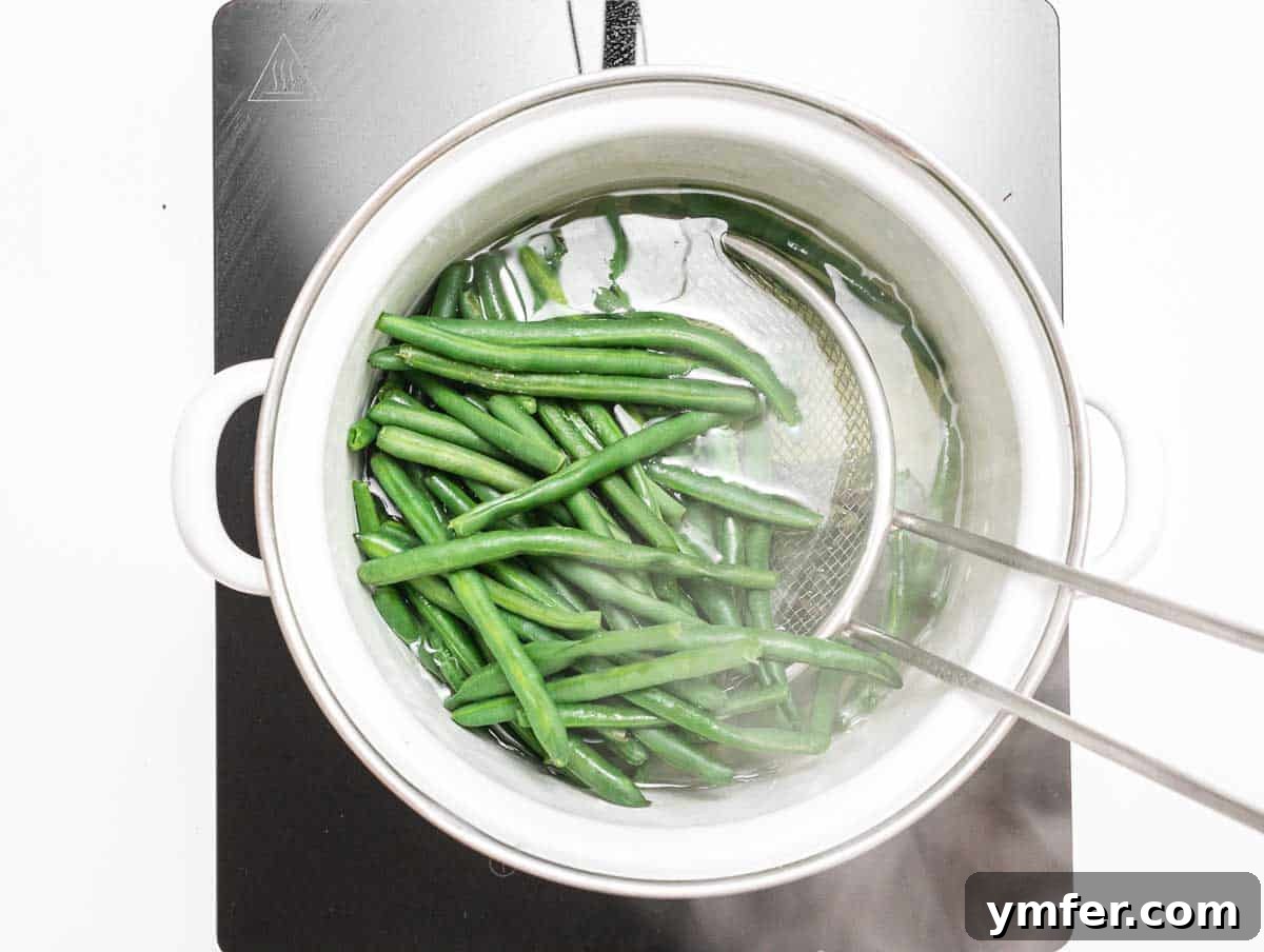 Flavorful Sautéed Green Beans 7 Vibrant green beans boiling in a white ceramic pot on a stovetop, capturing the moment of blanching