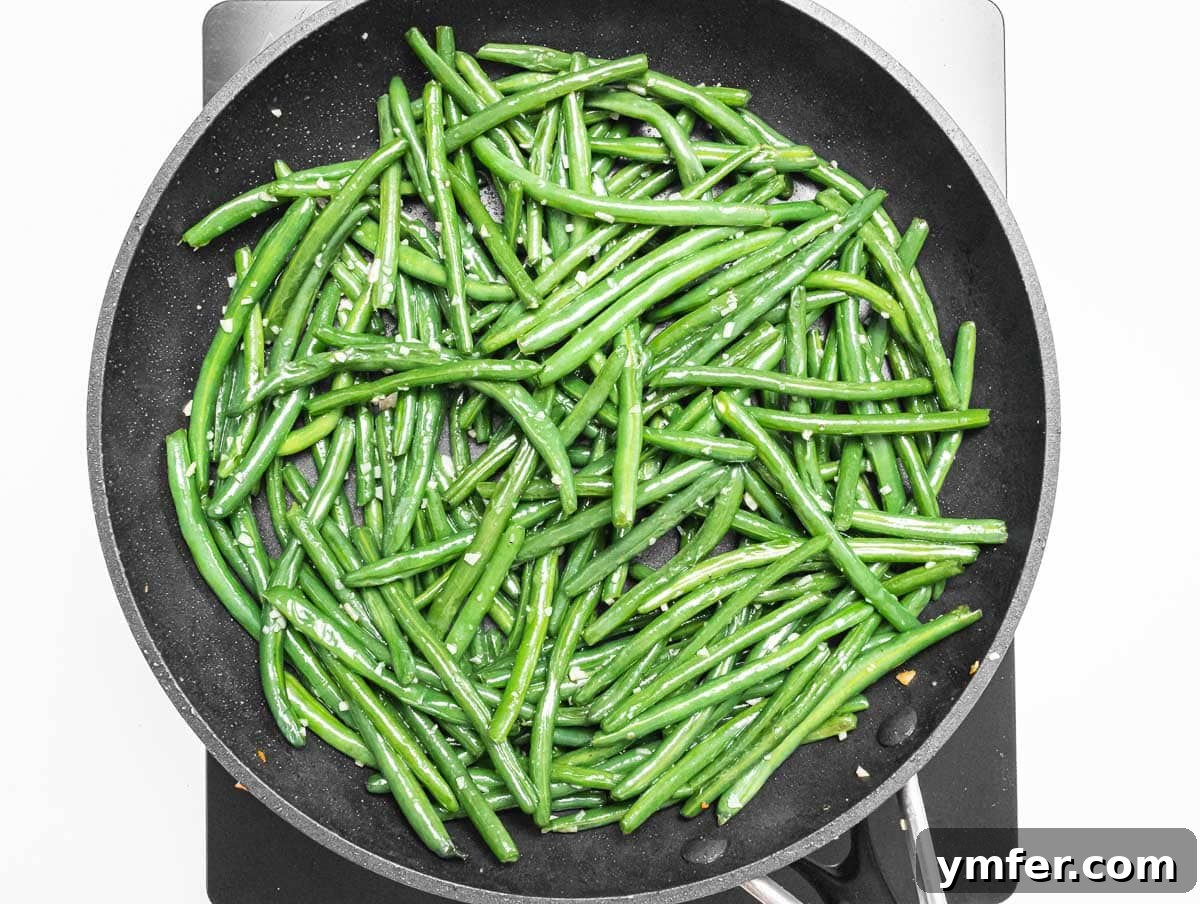 Flavorful Sautéed Green Beans 9 Fresh green beans being sautéed in a black pan with garlic and olive oil, in mid-toss for even cooking