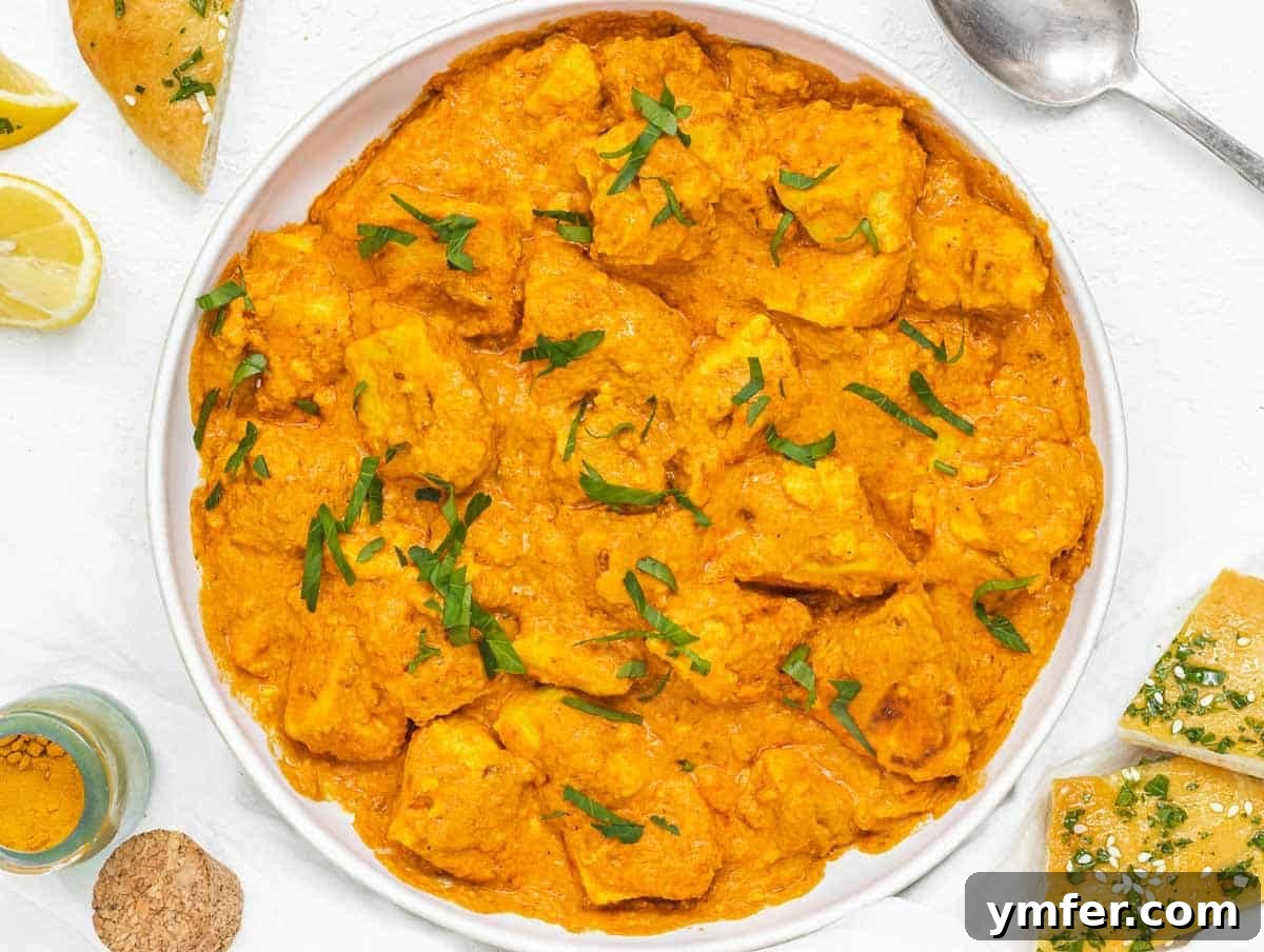 Velvety Vegan Butter Chicken 12 A serving of Vegan Butter Chicken garnished with fresh cilantro and lemon wedges, with naan bread on the side.