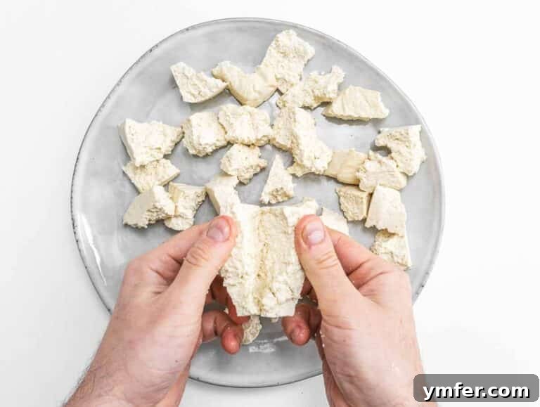 Velvety Vegan Butter Chicken 16 Hands carefully tearing a block of tofu into uneven pieces.