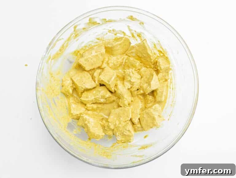 Velvety Vegan Butter Chicken 17 Tofu pieces fully coated in a vibrant turmeric-colored marinade in a mixing bowl.