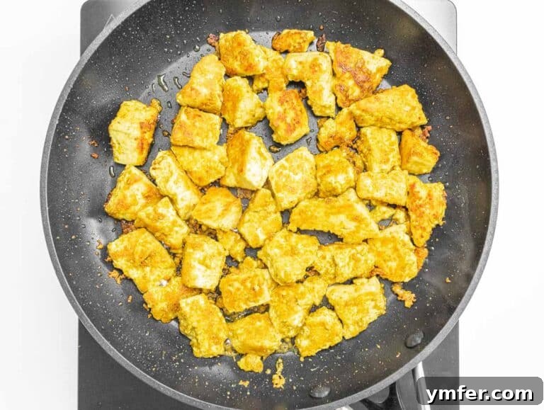 Velvety Vegan Butter Chicken 18 Golden yellow tofu pieces cooking in a hot pan, developing a crispy exterior.