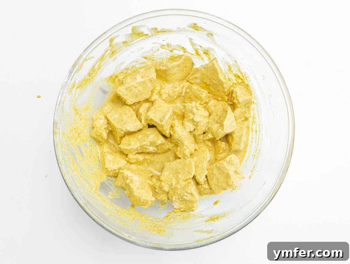 Velvety Vegan Butter Chicken 8 Tofu pieces coated in a vibrant turmeric-based marinade in a mixing bowl.
