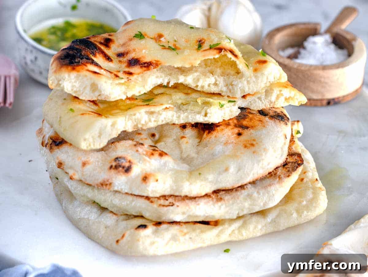 Pillowy Naan 16 A stack of golden brown naan breads on a white marble surface, showing their soft texture.