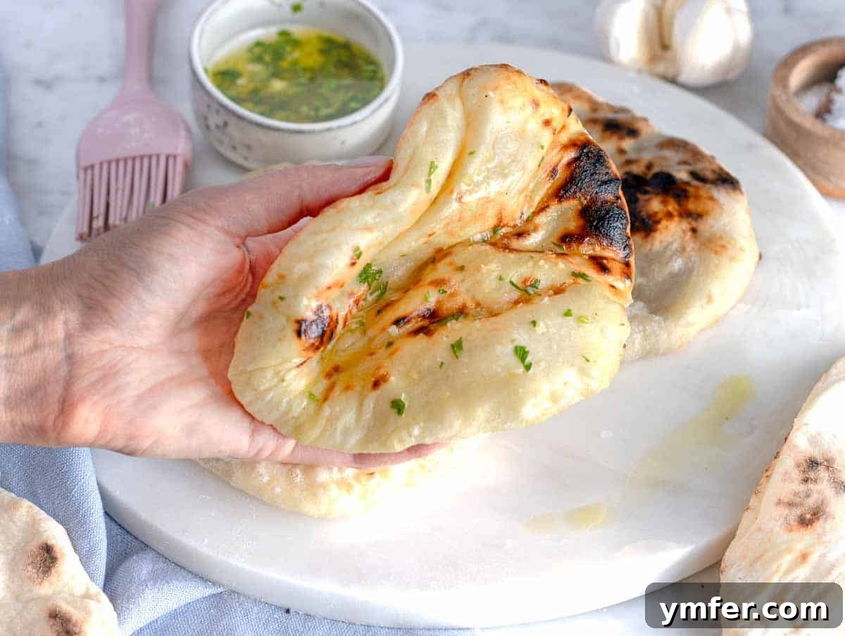 Pillowy Naan 3 A person holding a soft, freshly cooked naan bread, showcasing its flexible and fluffy texture.