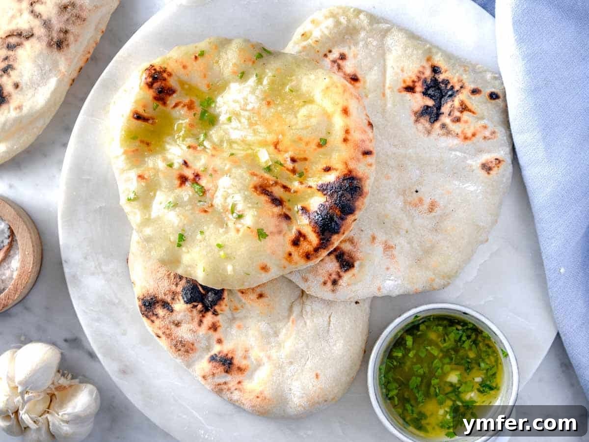 Pillowy Naan 4 Three golden-brown naan breads stacked on a wooden cutting board, brushed with olive oil and minced garlic.