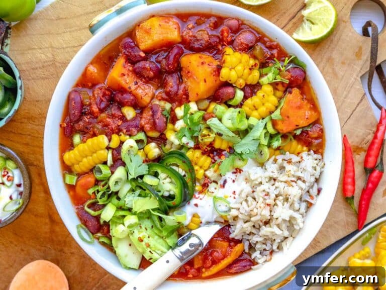 sweet potato chili in a bowl on rice and topped with jalapeños, cilantro, lime, sour cream, avocado, and corn.