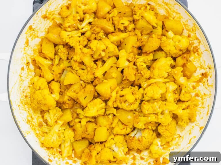 Cauliflower florets and potatoes being mixed into the sauce in a skillet.