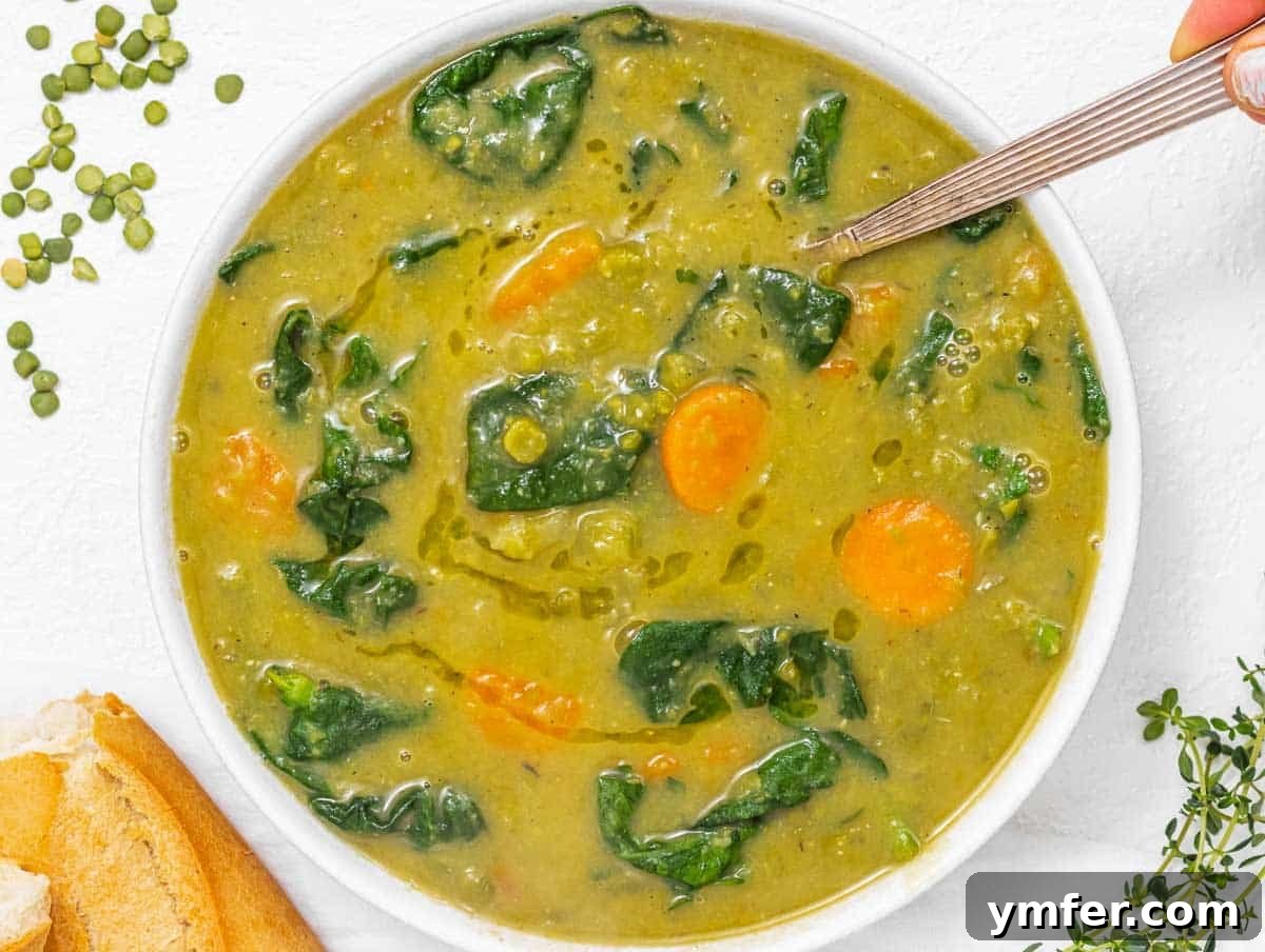 Golden Pea Goodness 12 A hand stirring a bowl of split pea soup with fresh spinach mixed in, adding a vibrant green color and extra nutrients, ready to be served with bread.