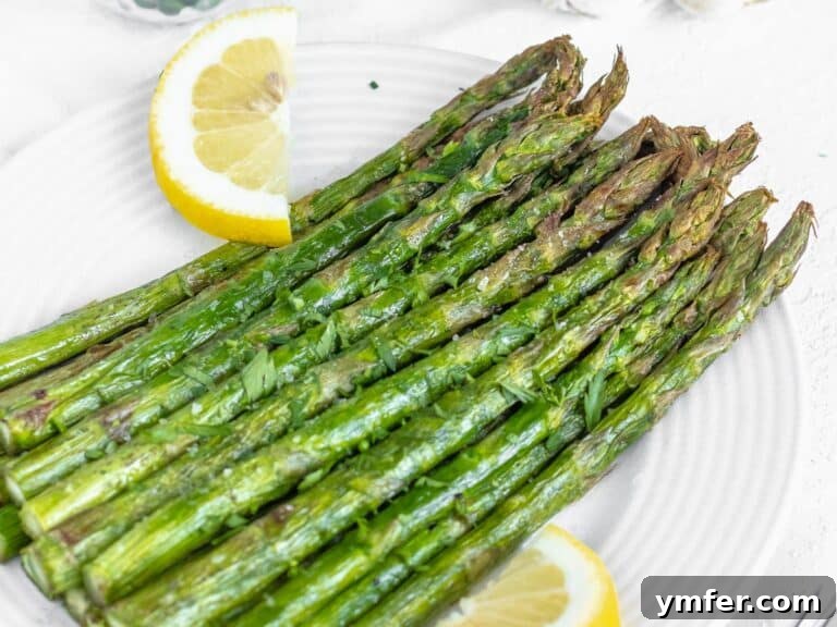 Effortless St Patricks Day Delights 23 Air fryer asparagus served on a plate with lemon wedges and fresh herbs.