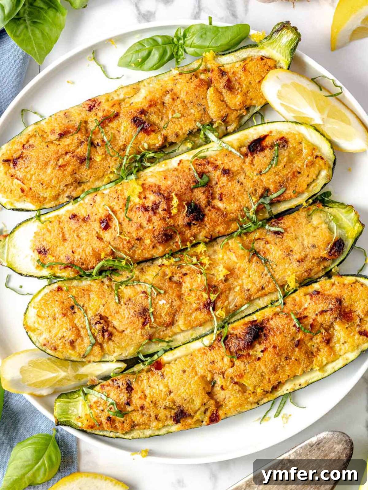 Cooked stuffed zucchini served on a plate, garnished with lemon and fresh basil.