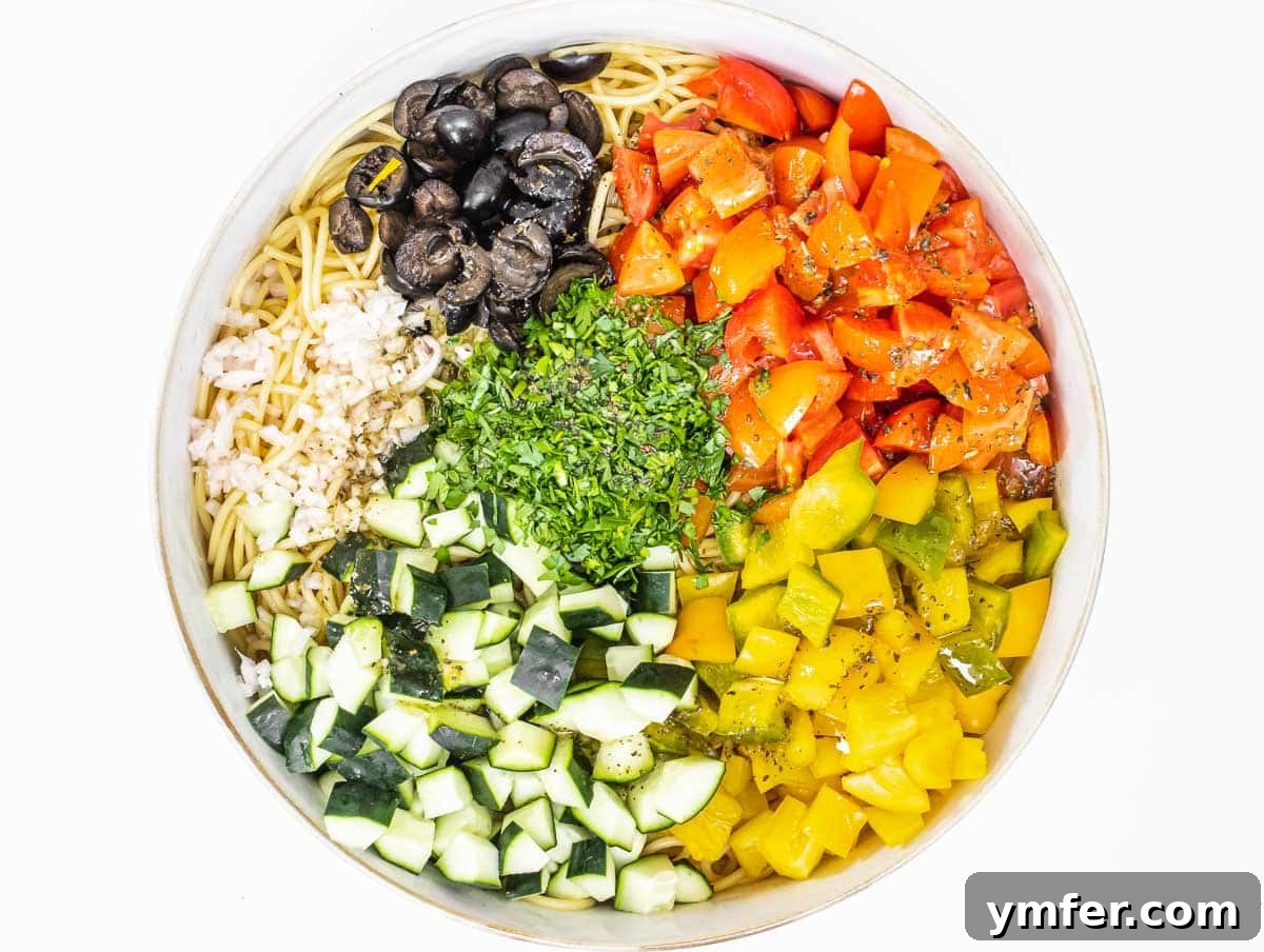 Vibrant Spaghetti Toss 7 A large bowl filled with cooked spaghetti and a vibrant mix of chopped fresh vegetables like tomatoes, cucumbers, and bell peppers.