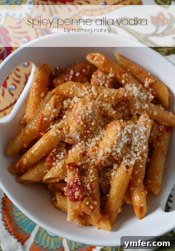 Spicy Penne Alla Vodka by Nutmeg Nanny A vibrant bowl of Spicy Penne alla Vodka, generously coated in a rich, orange-hued sauce, studded with savory prosciutto and fresh parsley. The dish is presented in a white bowl with a fork, emphasizing its inviting texture and warmth, perfect for a cozy meal.