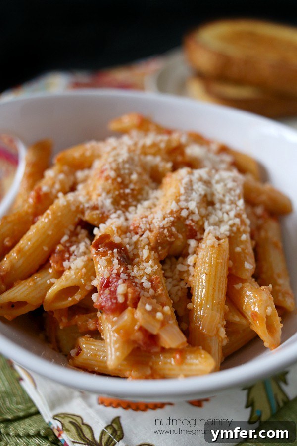 Spicy Penne Alla Vodka by Nutmeg Nanny A close-up shot of the creamy and rich Penne alla Vodka sauce, showcasing its vibrant orange hue, flecks of red pepper, and tender pieces of prosciutto. The sauce glistens, indicating its smooth texture, while the pasta beneath is perfectly coated, inviting a delightful culinary experience.