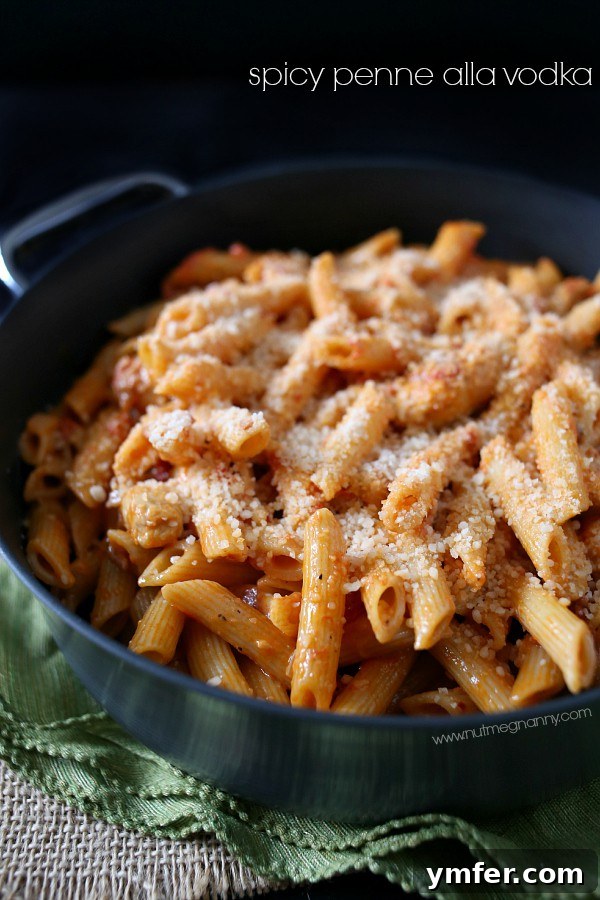 Spicy Penne Alla Vodka by Nutmeg Nanny A beautifully presented bowl of Spicy Penne alla Vodka, garnished with fresh parsley and grated Parmesan cheese, sits on a rustic wooden surface. The vibrant colors of the sauce and pasta are enhanced by the warm lighting, suggesting a comforting and inviting meal ready to be enjoyed.