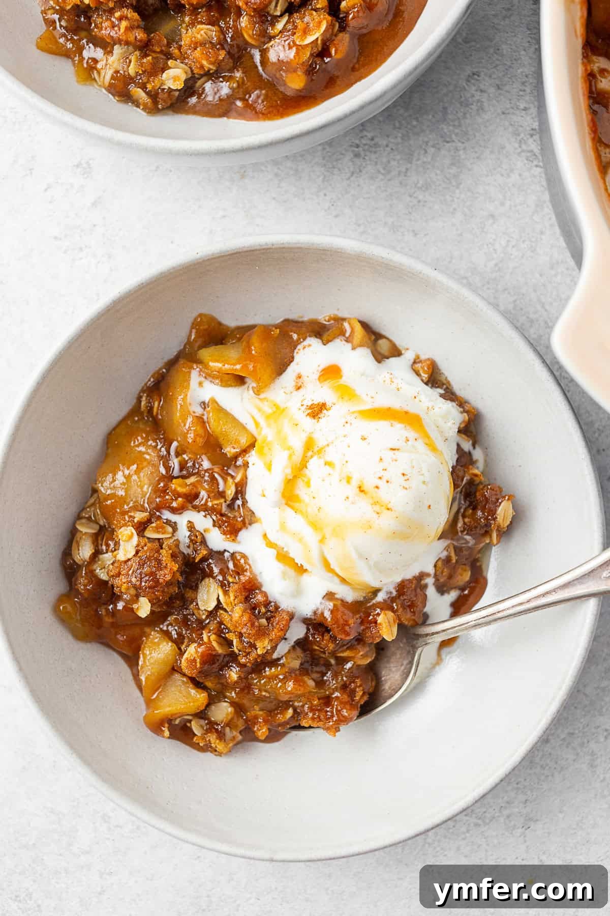 Sticky Caramel Apple Delight 2 A bowl filled with caramel apple crisp topped with ice cream, ready to be enjoyed.