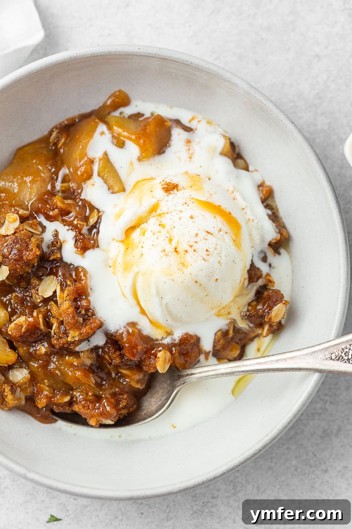Sticky Caramel Apple Delight 6 Easy caramel apple crisp in a bowl with a spoon and melted vanilla ice cream, showing the gooey caramel.