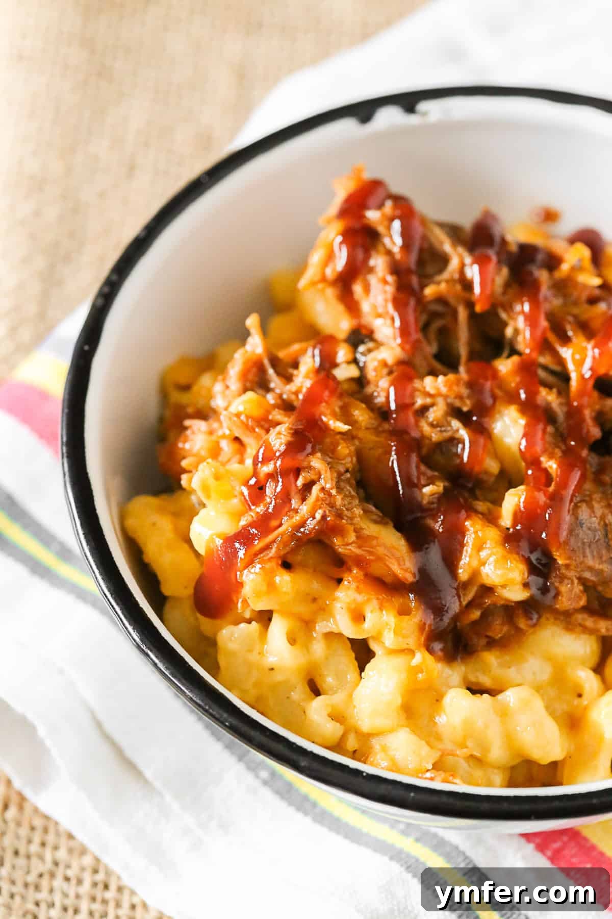 A bowl of pulled pork mac and cheese topped with a generous drizzle of BBQ sauce.