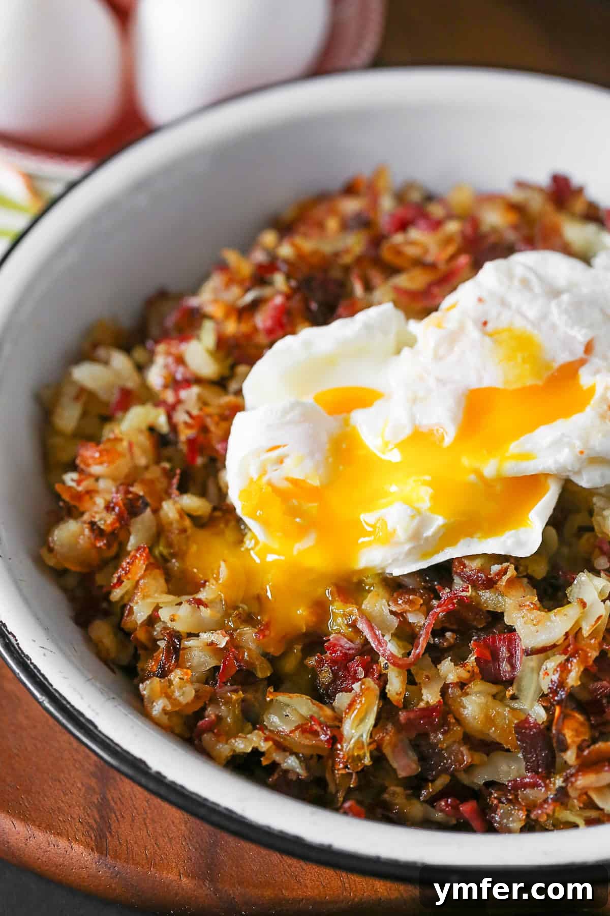 A vibrant plate of corned beef hash featuring crispy potatoes, savory corned beef, and tender cabbage, crowned with a perfectly poached egg whose yolk gracefully spills onto the hash.