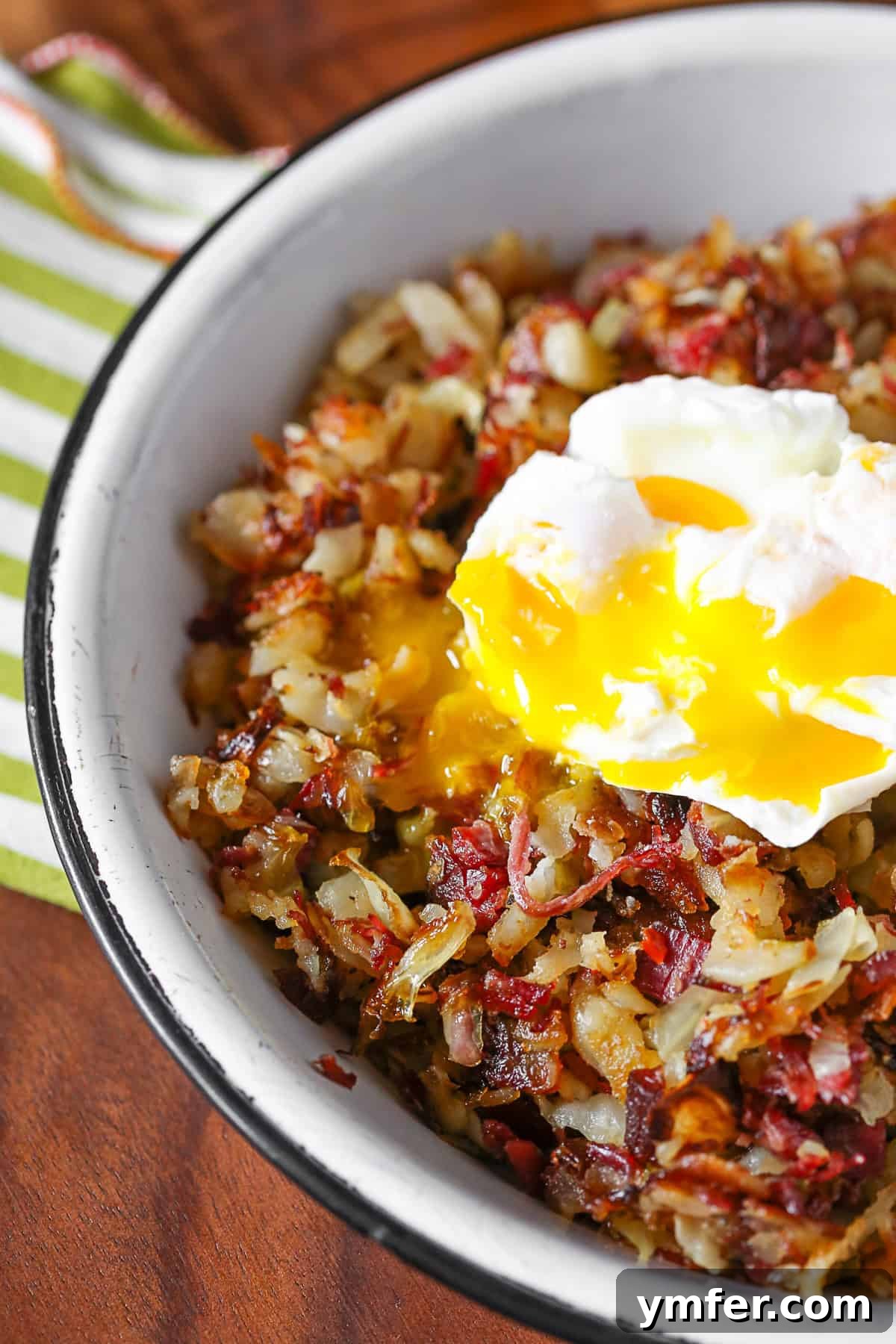 A rustic bowl of crispy corned beef hash, beautifully topped with a perfectly cooked poached egg, ready to be broken open for a creamy yolk.