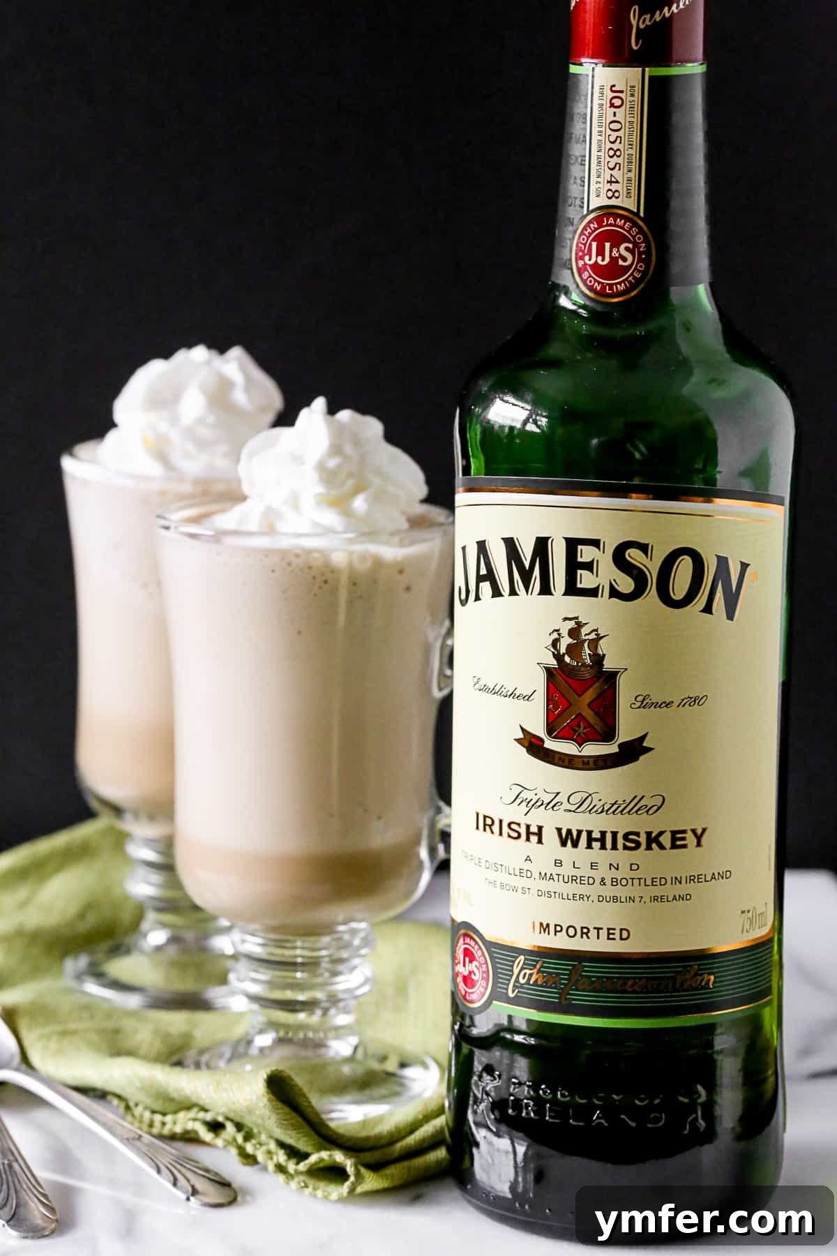 Irish Coffee Frappe by Nutmeg Nanny A single glass of Irish Coffee Frappe on a rustic table, with a bottle of Irish whiskey and a few coffee beans scattered around, hinting at its key ingredients.