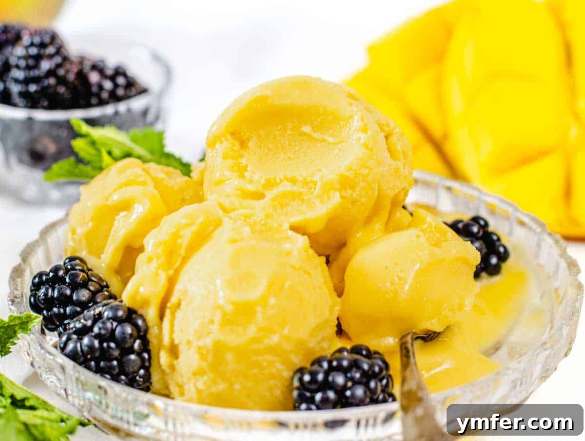 Scooped mango sorbet in a bowl with a spoon, garnished with berries.