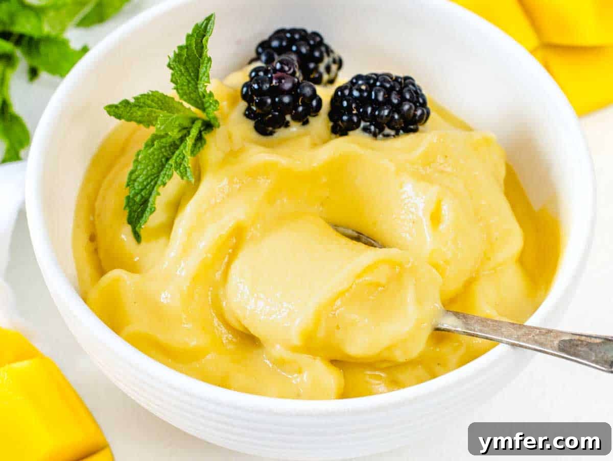 A bowl of creamy soft-serve mango sorbet with a silver spoon, ready to be eaten.