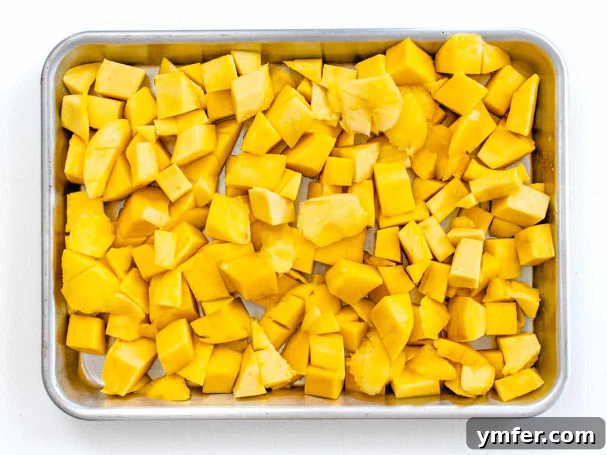 Frozen mango chunks spread on a baking sheet, ready for blending.