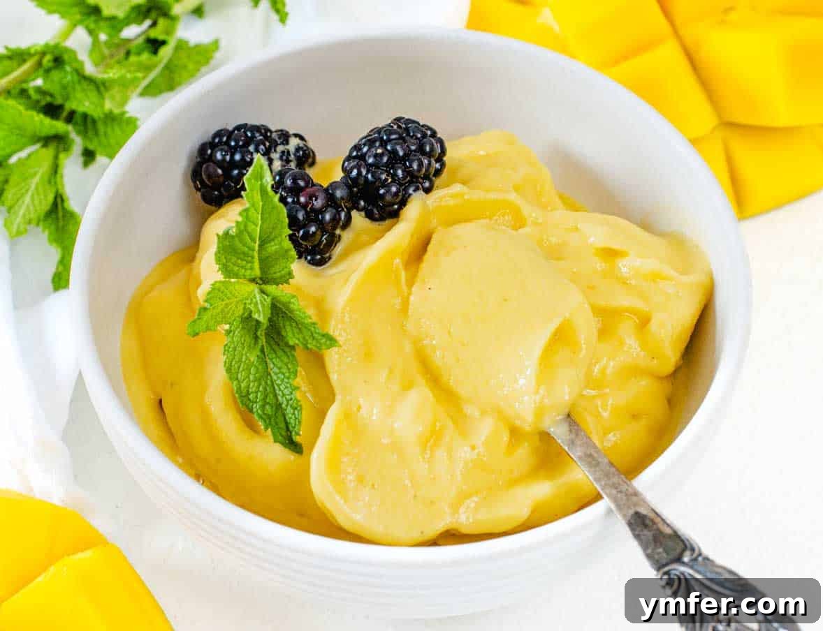 A bowl of soft-serve mango sorbet garnished with blackberries and mint leaves.