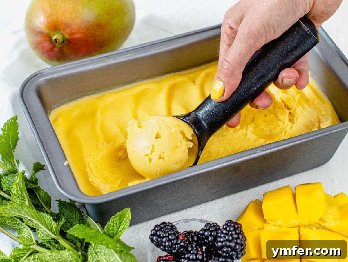 A hand scooping frozen mango sorbet from a loaf pan.