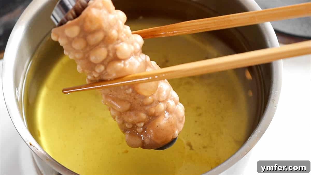 Freshly deep-fried cannoli shell cooling on a rack.