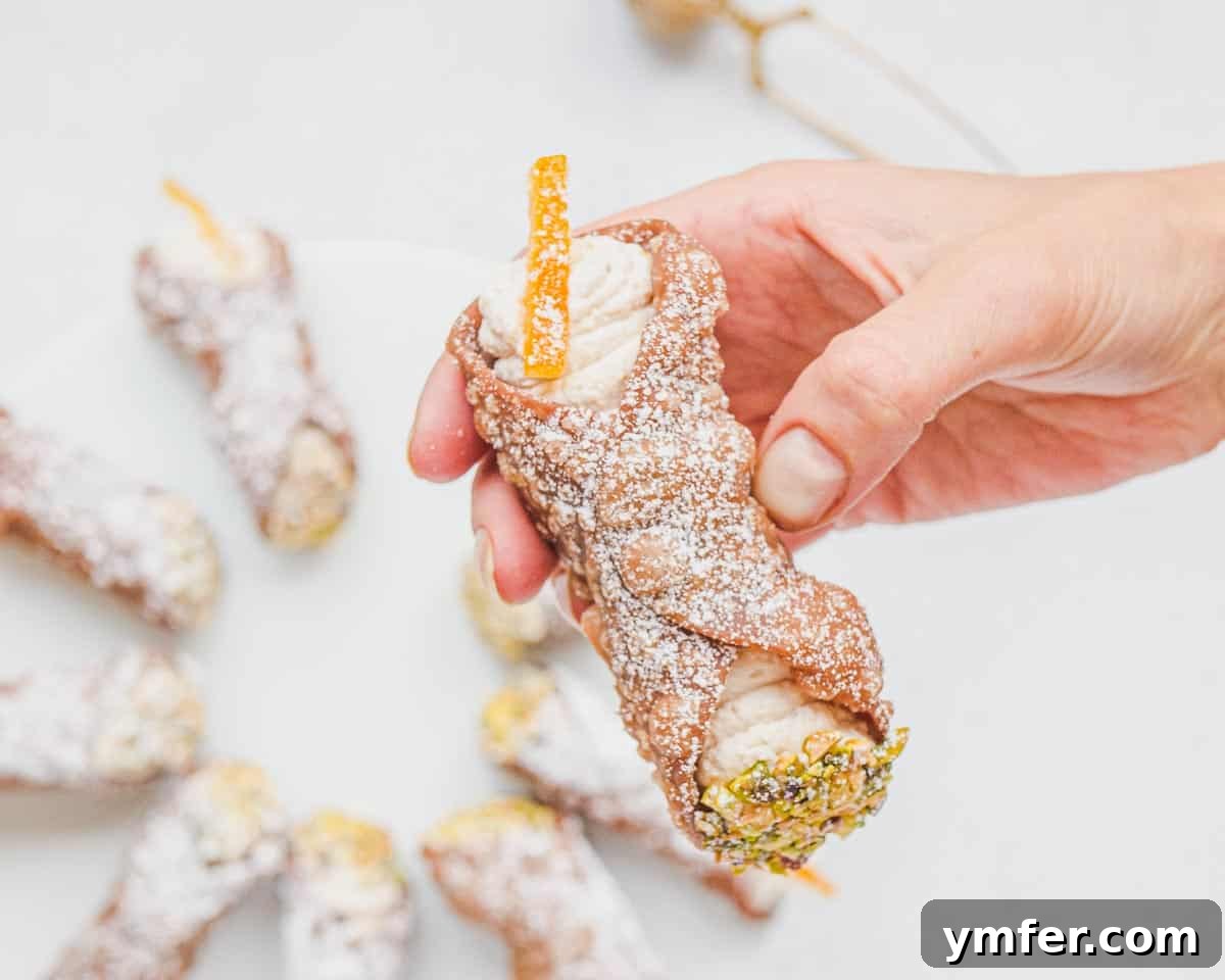 A person holding a perfectly filled and garnished vegan cannolo.