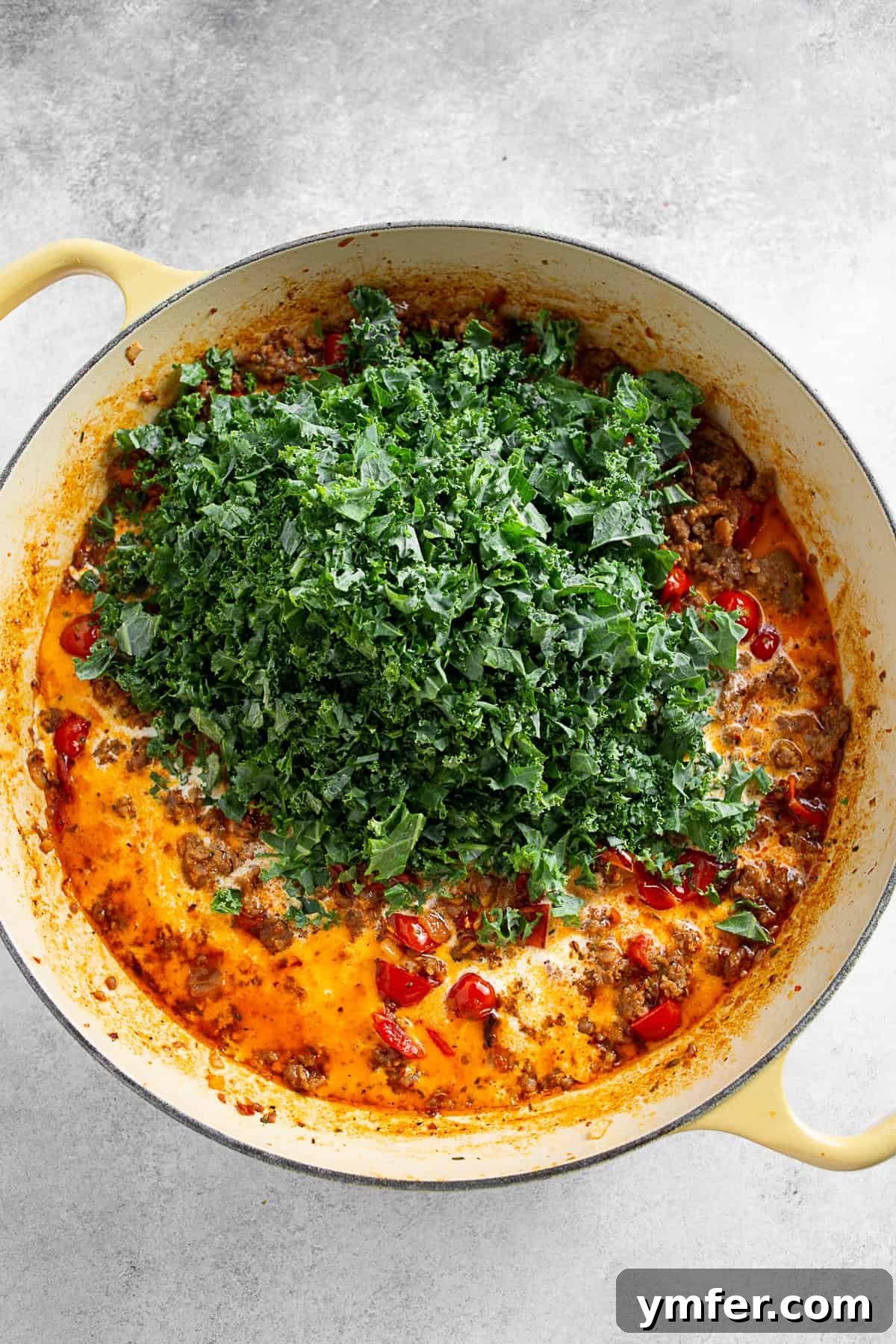 Adding kale to a skillet of creamy tomato sauce. 
