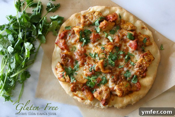 Indian-Inspired Gluten-Free Chicken Tikka Masala Pizza 4 A slice of Gluten-Free Chicken Tikka Masala Pizza being lifted, showcasing the crispy crust and flavorful toppings.