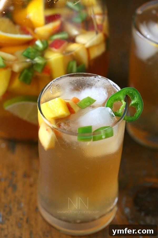 Spicy Hibiscus Peach Tea Sangria being poured from a pitcher into a glass with fruit and ice