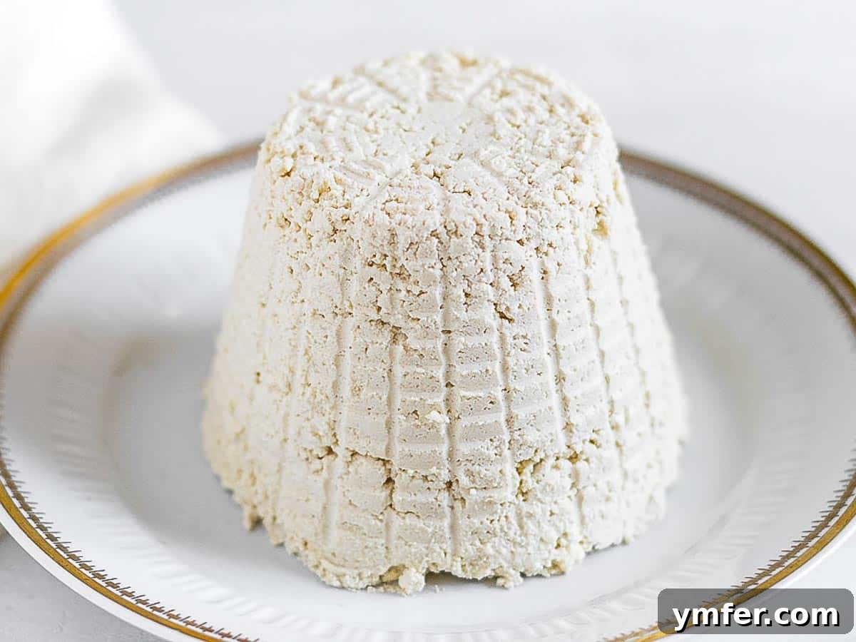 Creamy Vegan Ricotta 14 A beautifully shaped vegan ricotta cheese, just removed from its mold, sitting on a white plate.