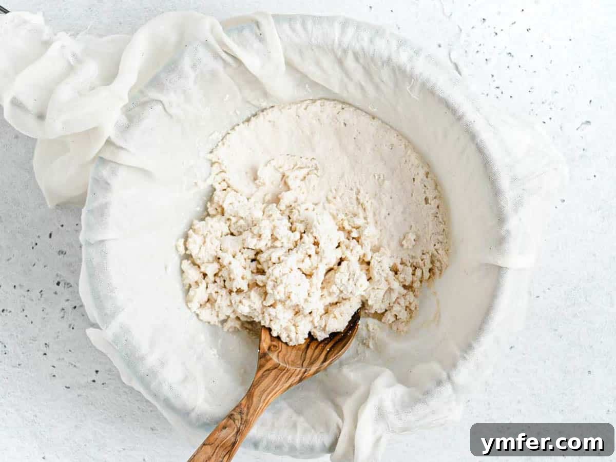 Creamy Vegan Ricotta 4 Dairy-free ricotta being drained in a fine-mesh sift, with a wooden spoon nearby, highlighting the traditional cheesemaking process.