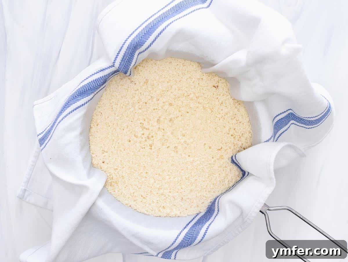 Creamy Vegan Ricotta 10 Curdled soy milk poured into a strainer lined with a cloth, with whey visibly draining into the bowl below.