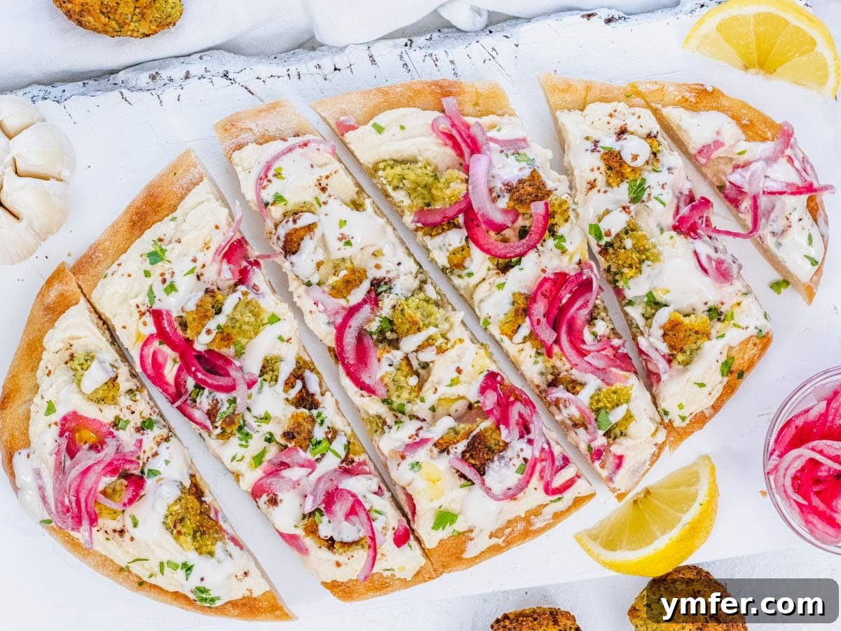 Flatbread pizza with hummus, falafel, tahini sauce, and pickled onions