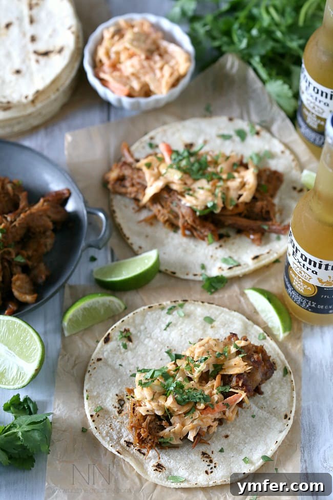 These slow cooker ginger beer pulled pork tacos are topped with a spicy chipotle cole slaw and served on toasted corn tortillas. A plate of Ginger Beer Pulled Pork Tacos, ready to be enjoyed.