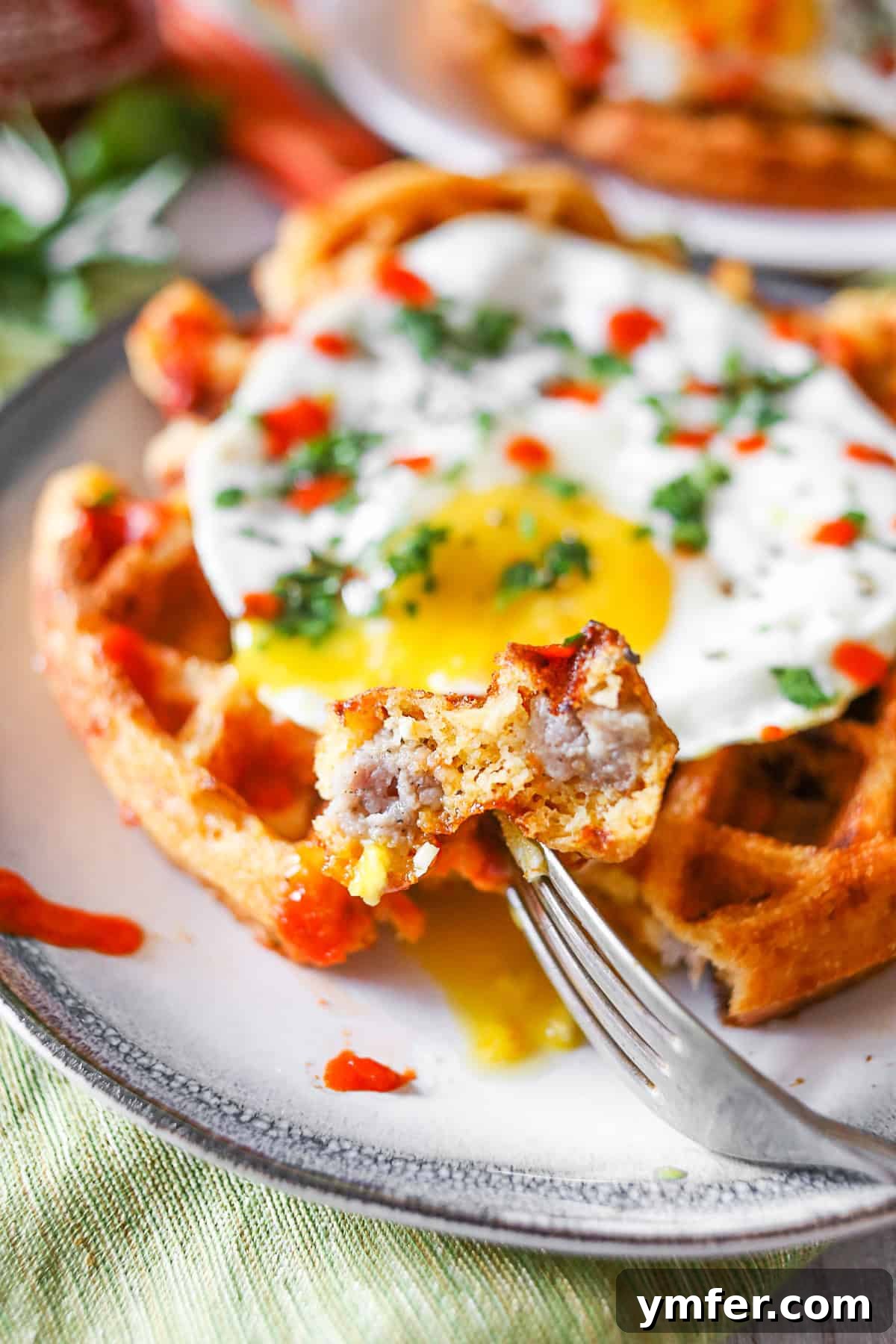 Enjoy a close-up of a delightful Cheddar Sausage Cornmeal Waffle, revealing its rich ingredients. A slice of Cheddar Sausage Cornmeal Waffle on a fork, showing its delicious texture.