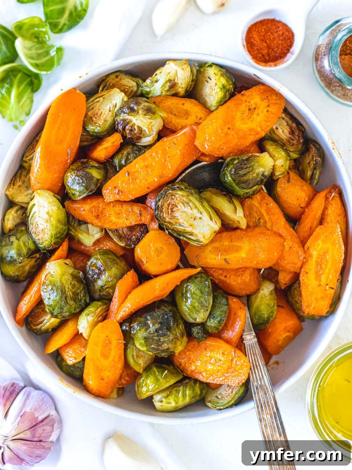 Caramelized Carrots and Crispy Brussels Sprouts 2 Roasted carrots and Brussels sprouts in a white bowl with a spoon, garnished with fresh herbs.