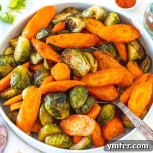 A serving bowl of roasted carrots and Brussels sprouts, ready to eat.