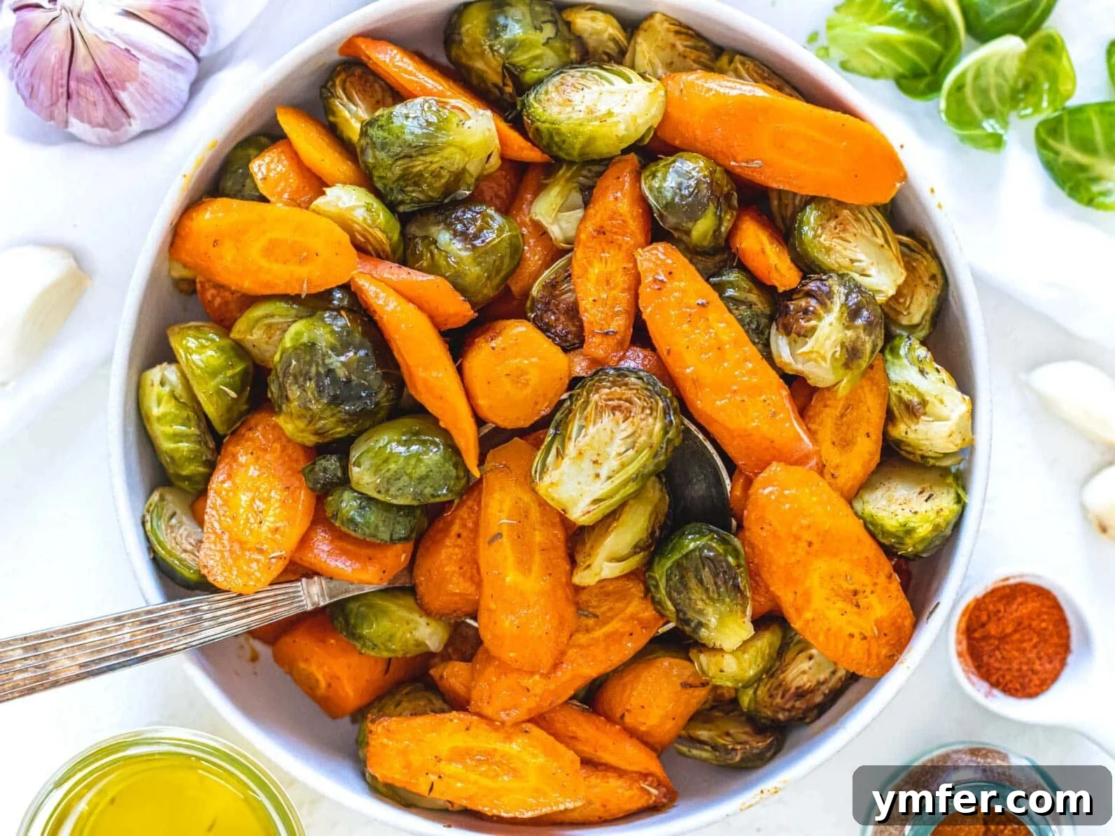 Caramelized Carrots and Crispy Brussels Sprouts 10 A large white bowl filled with roasted carrots and Brussels sprouts, garnished, with a serving spoon.