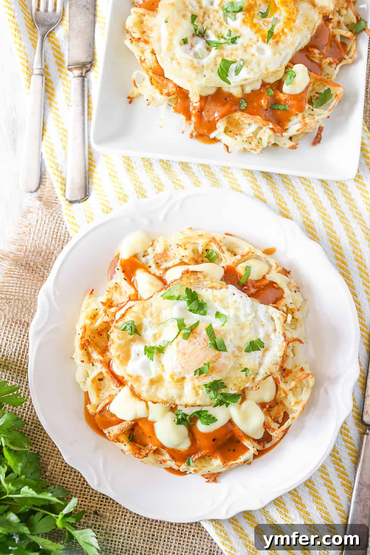 These crispy poutine hash brown waffles are the perfect way to start the day. Crispy potato waffles, homemade gravy, cheese curds and a fried egg. Hello breakfast! Two plates of Poutine Hash Brown Waffles, topped with gravy, cheese curds, and fried eggs. Perfect for breakfast or brunch.