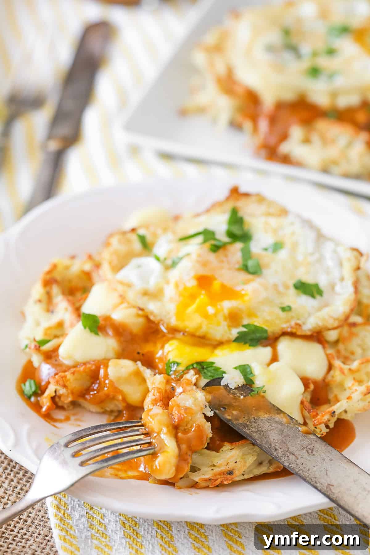 These crispy poutine hash brown waffles are the perfect way to start the day. Crispy potato waffles, homemade gravy, cheese curds and a fried egg. Hello breakfast! A knife and fork cutting into a crispy Poutine Hash Brown Waffle, revealing its delicious layers of gravy and cheese curds.