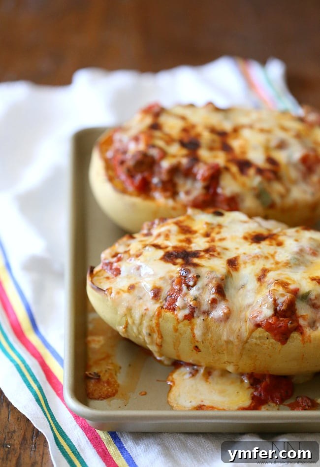 Savory Sausage and Pepper Spaghetti Squash Bake 3 Two halves of Sausage and Peppers Stuffed Spaghetti Squash resting on a baking sheet, ready for the oven. The golden-brown sausage and vibrant peppers peek out from beneath a generous layer of melted, bubbly mozzarella cheese.